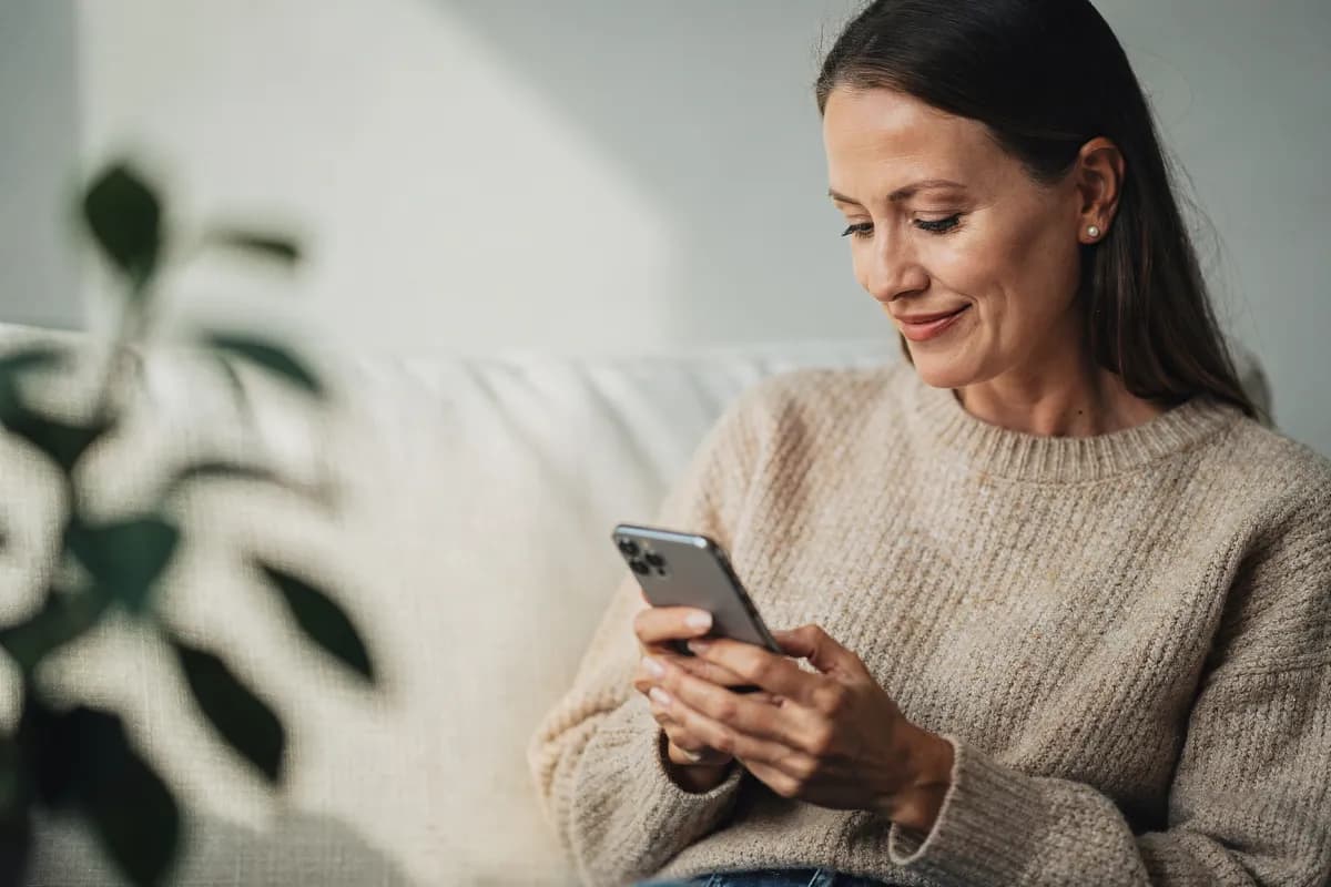 A woman relaxing at home, sending a refill request from her phone